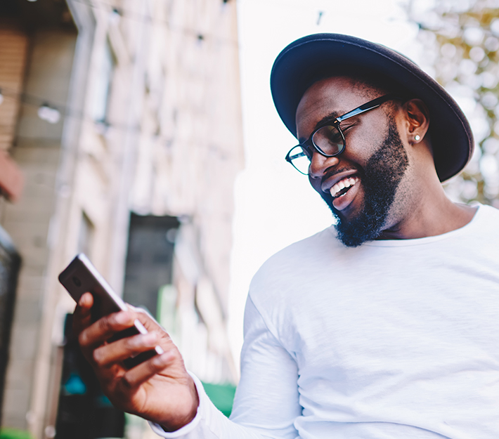 Man with hat, smiling and looking at phone.