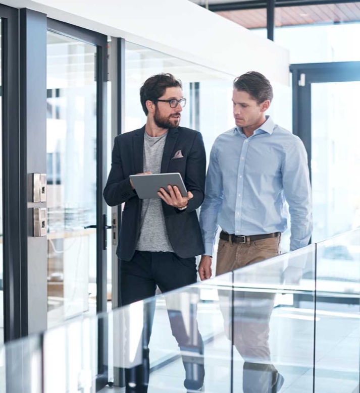 Two business people walking and talking, looking at tablet.