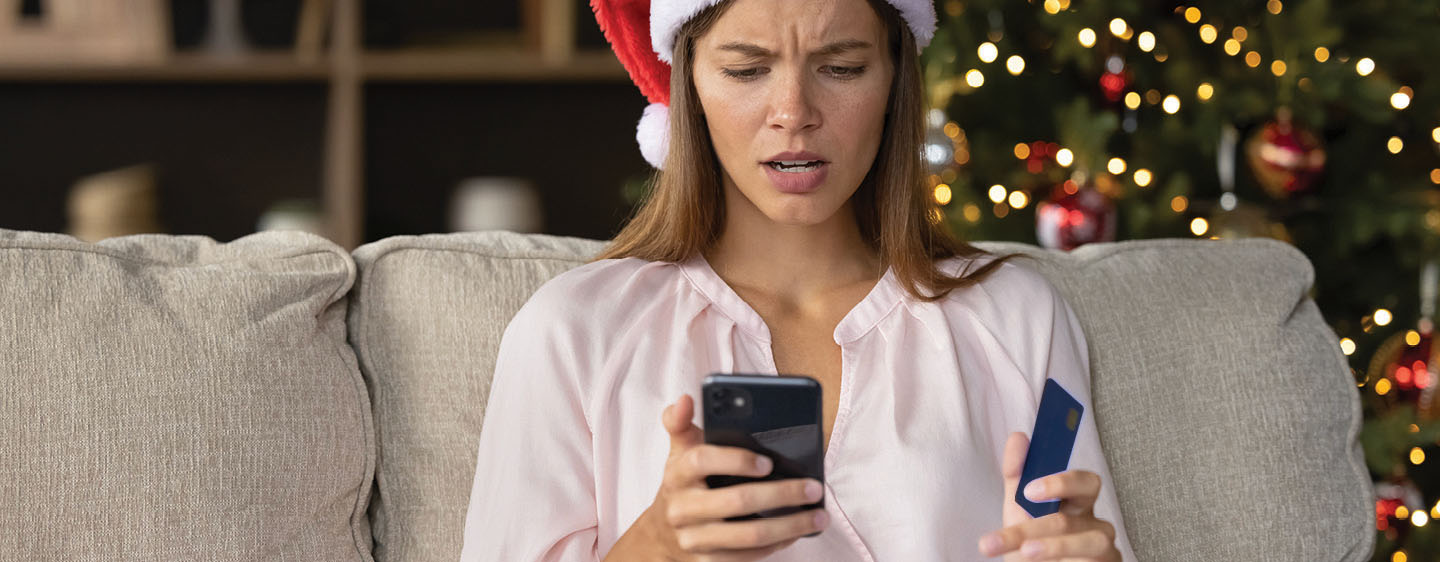 Woman with a disappointed look on her face looking at her phone and holding a credit card.