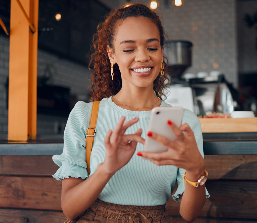 Image of a woman at a coffee shop smiling at her phone.