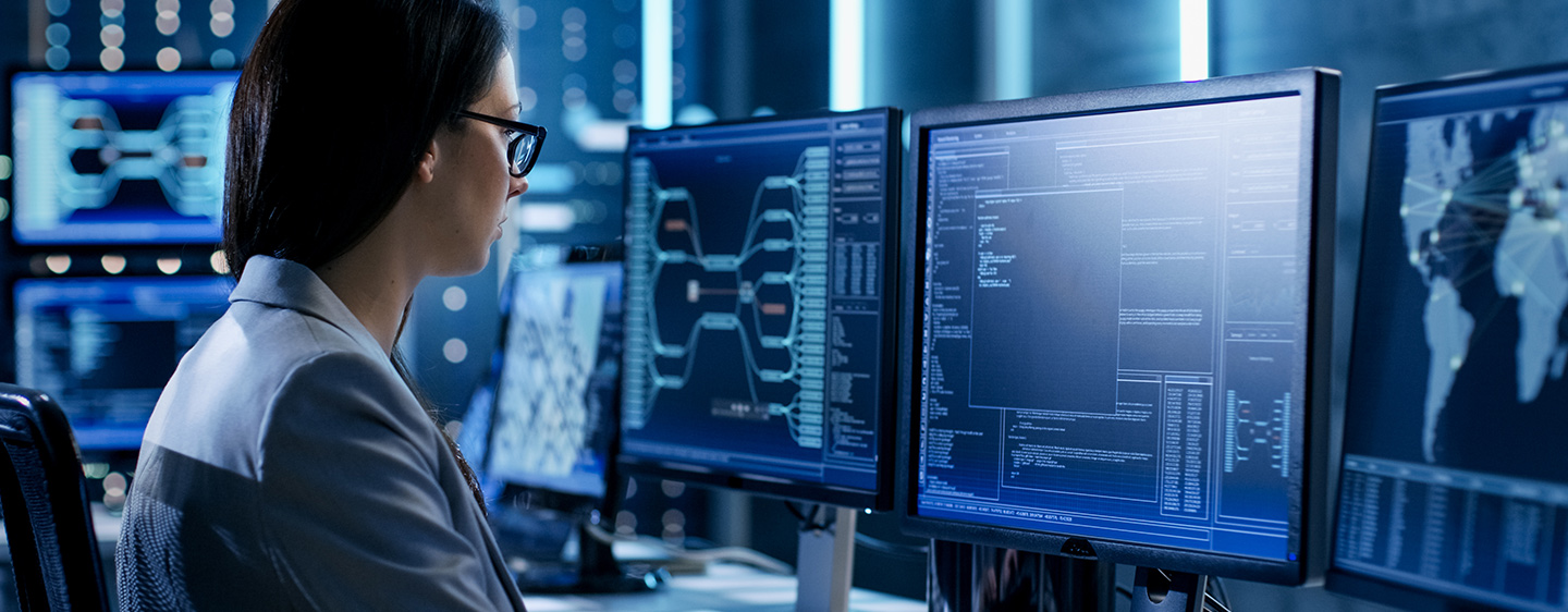 Person looking at complicated computer monitors, monitoring fraud.