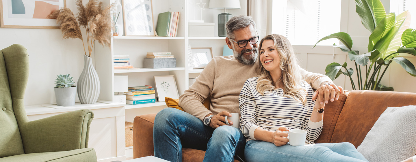 Man and woman sit on a couch together, enjoying coffee.