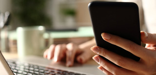 Image of a woman using a laptop and a cell phone.