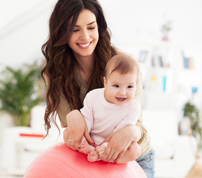 Mother holds baby on an exercise. ball.