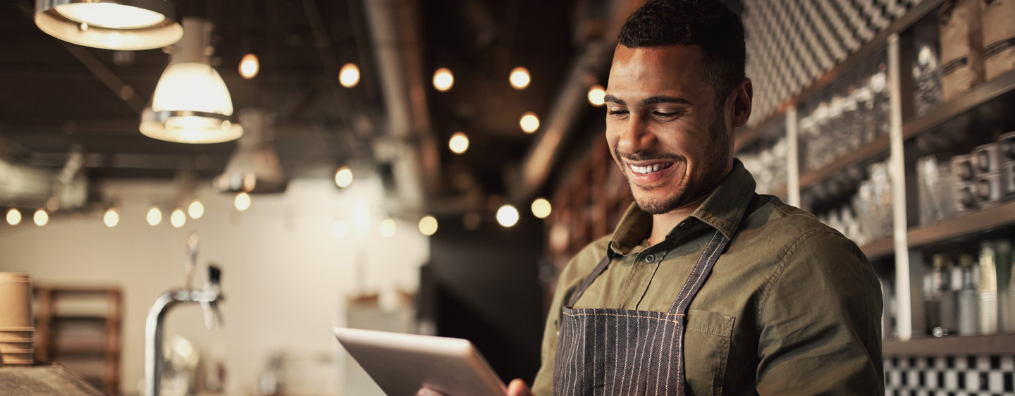 A business owner in an apron smiles at a tablet.