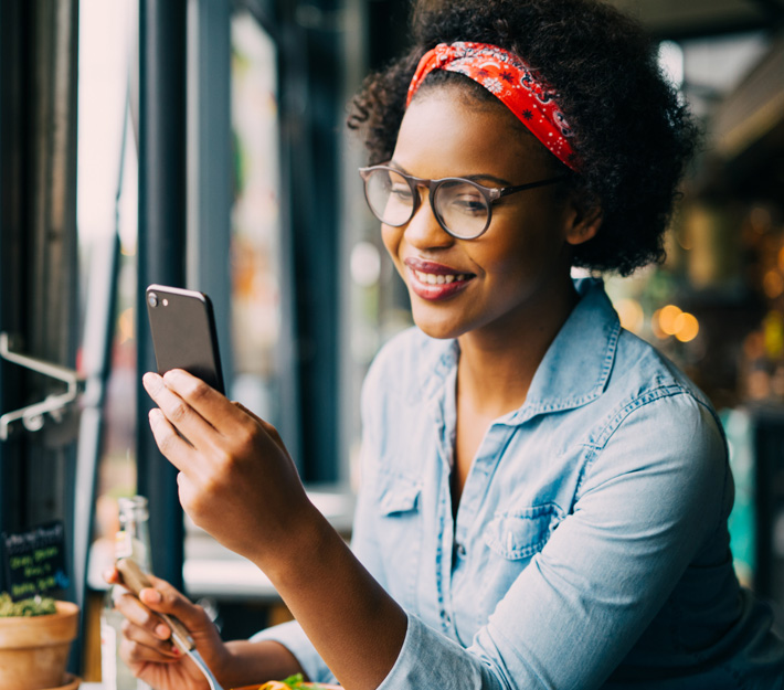 A young woman smiles as she surfs the web on her phone.