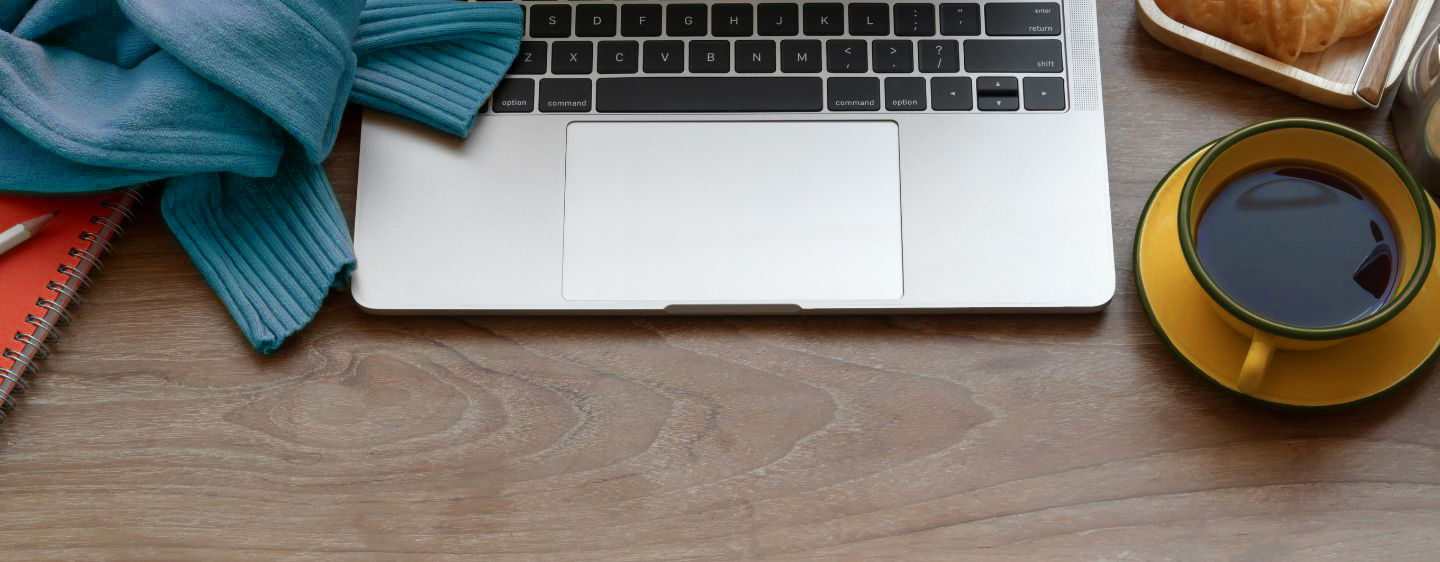 Image of a computer, coffee cup, sweater, and notebook on a desk.