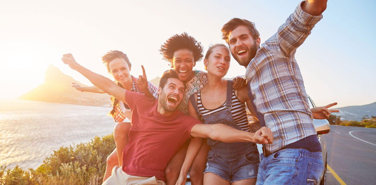 A group of friends pose together in front of a car during a road trip.