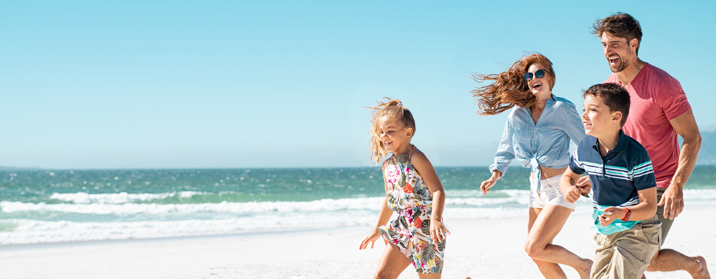 Image of a family on vacation, running on the beach together in the sunshine.