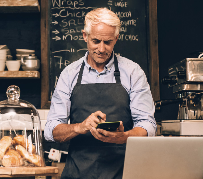 Business owner stands at the register of his business with a tablet.