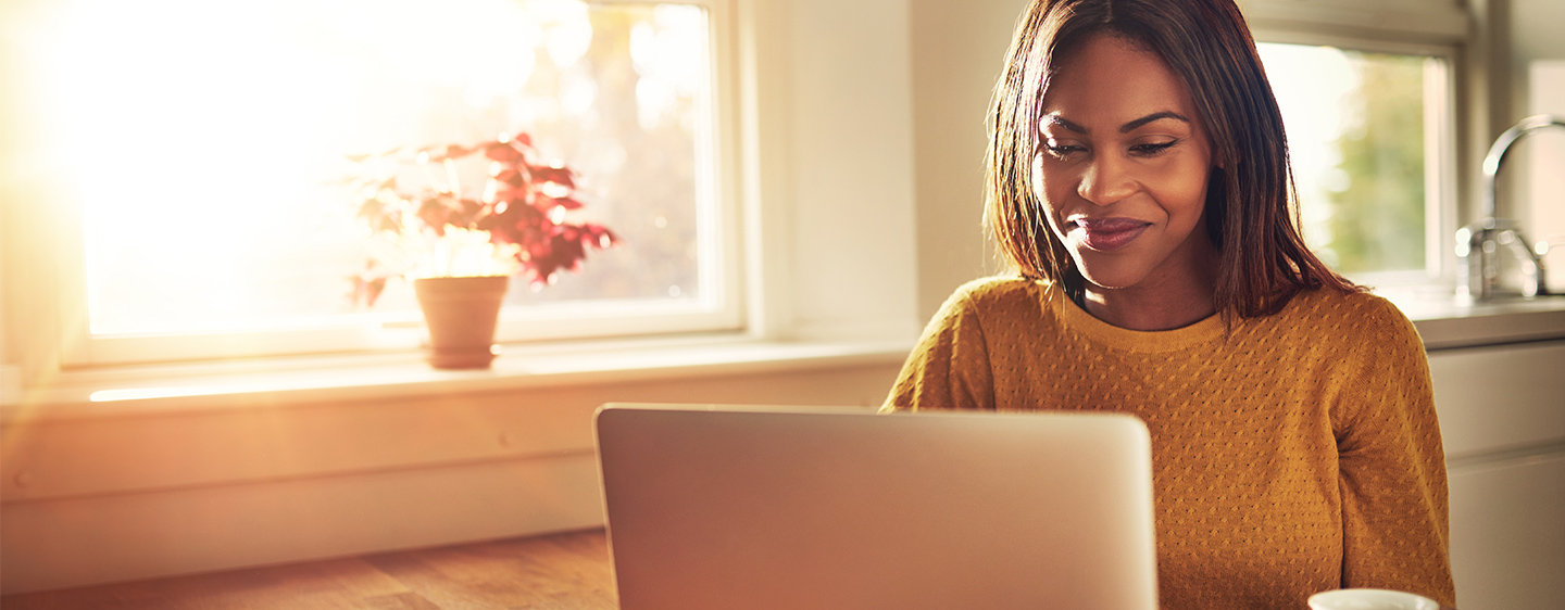 Women wearing an orange sweater looking at her laptop.