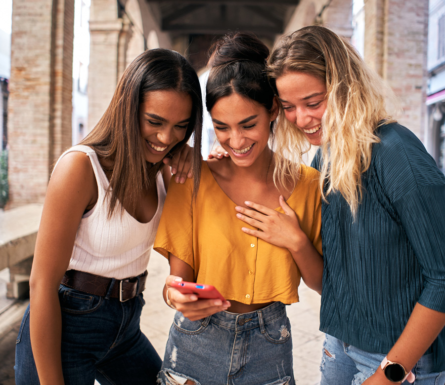 3 millennial women smile at a cell phone