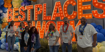 An image of CCU team members in front of a lit up sign that reads Best Places to Work