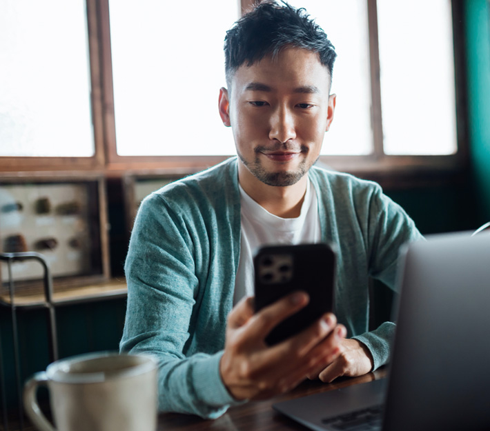 Image of a man at his laptop using a cell phone