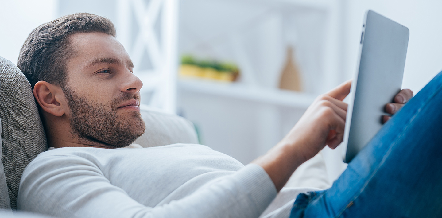 Man lying on the couch using a tablet.