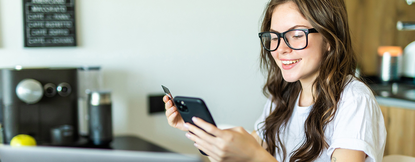 Young woman smiling with glasses typing card number into phone.