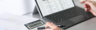 A close-up of a client in a business suit holding a pen to sign a contract on a clipboard while a loan officer points to the signature line, representing the approval process for summit financial loans.