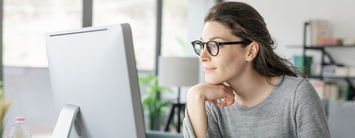 Woman in glasses smiles slightly at her computer