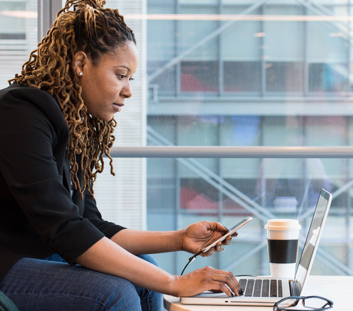 Woman using a cell phone and looking at a laptop.