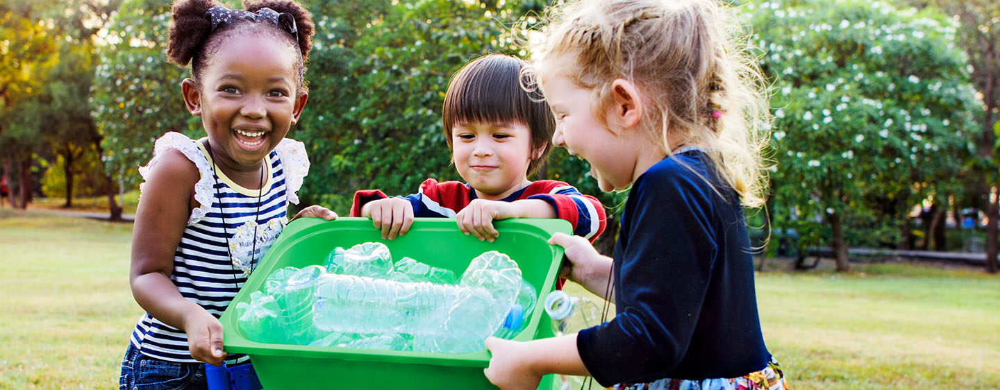 3 small girls carrying a container of recycling.