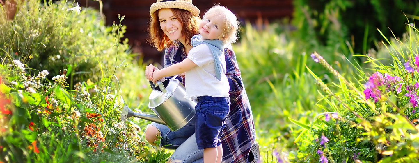 Mother and daughter water flowers outside in a garden.