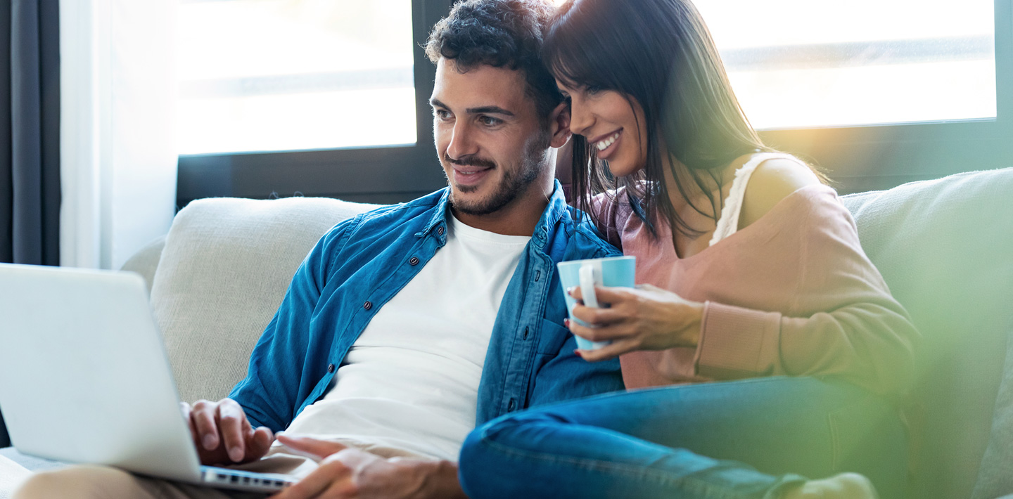 Man and woman sit together on a couch and view a laptop.