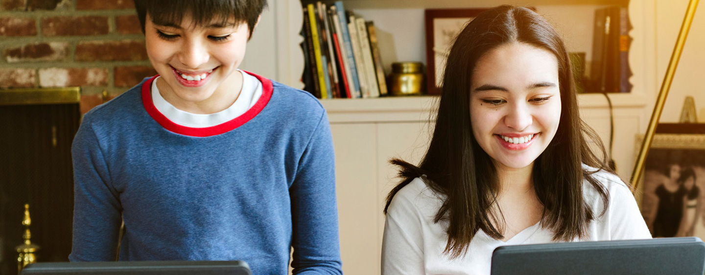 Two tweens smile as they use computers.
