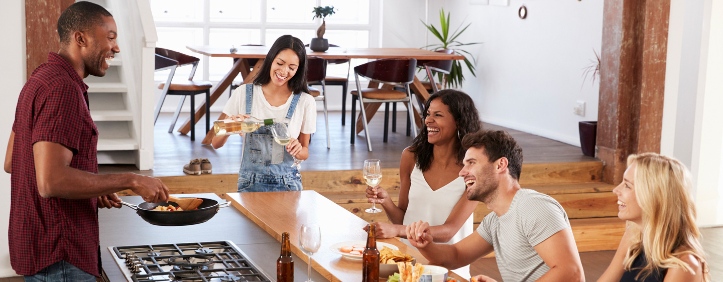 Group of friends laugh together as food is being prepared.