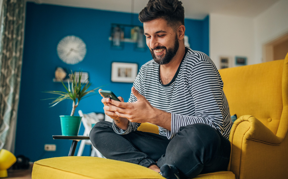 Man sitting in yellow arm chair looking at his phone.