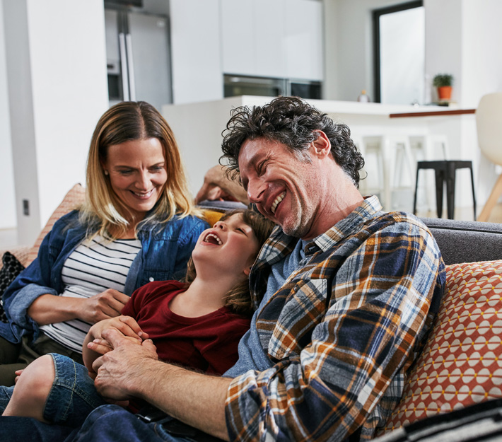 Mom, dad, and daughter laughing on the couch.