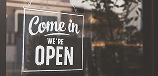Picture of a business window with a sign that says come in we're open.