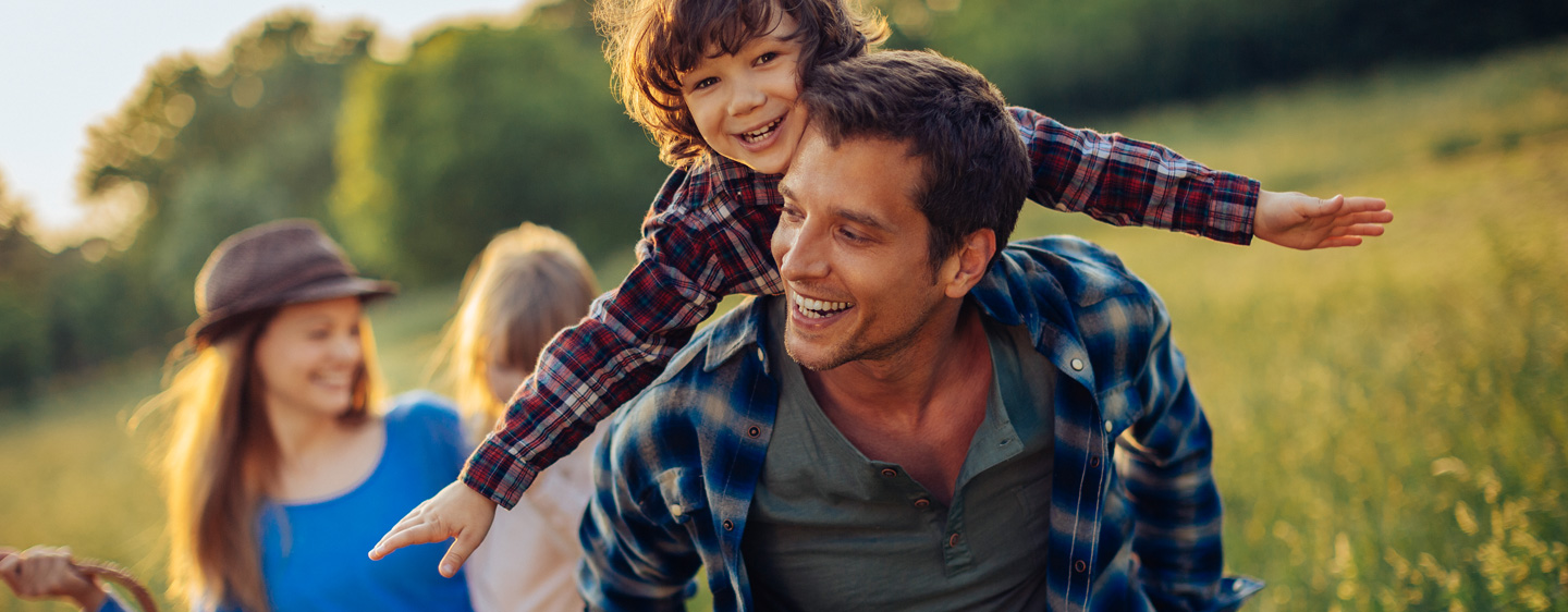 Family playing in a field. Child on dad's back flying.