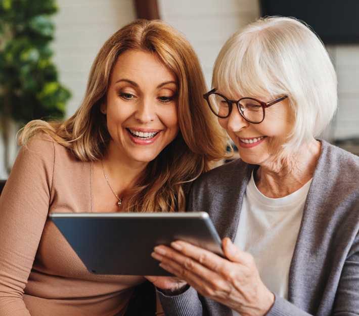 An elderly woman and her daughter view a tablet together.