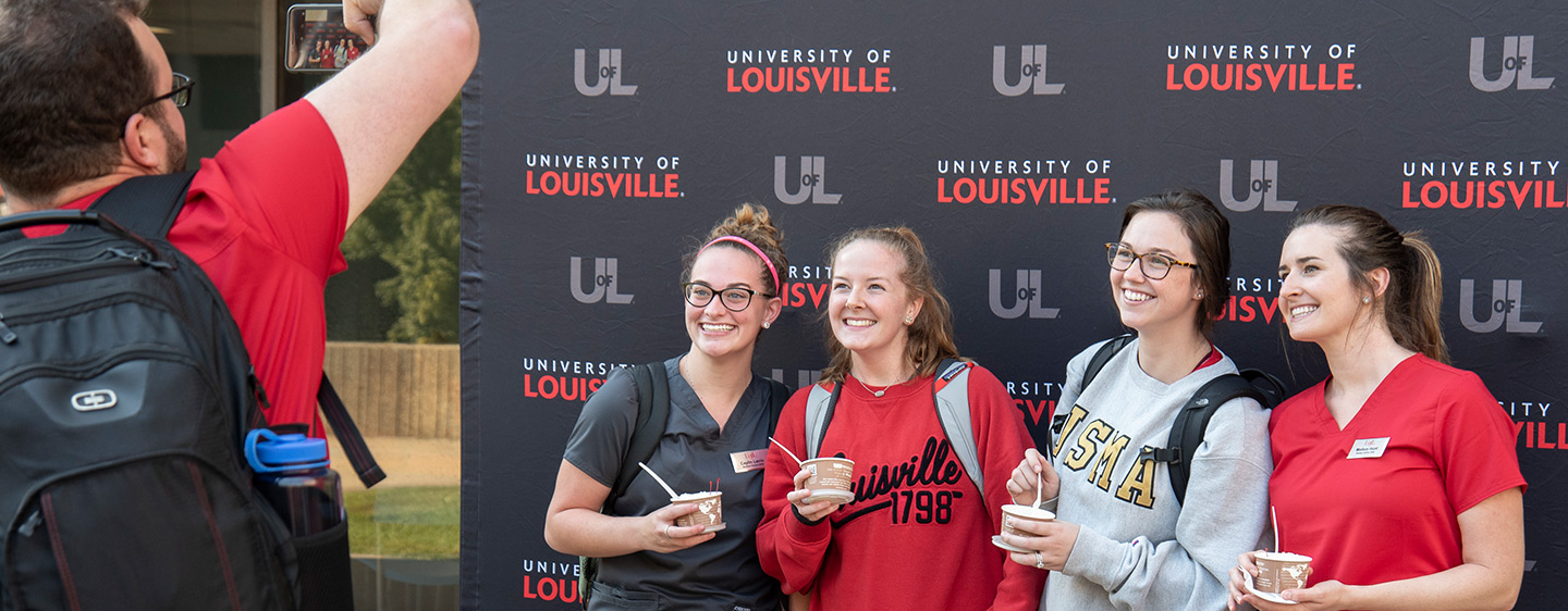 People getting their photo taken in from of a U of L step and repeat.