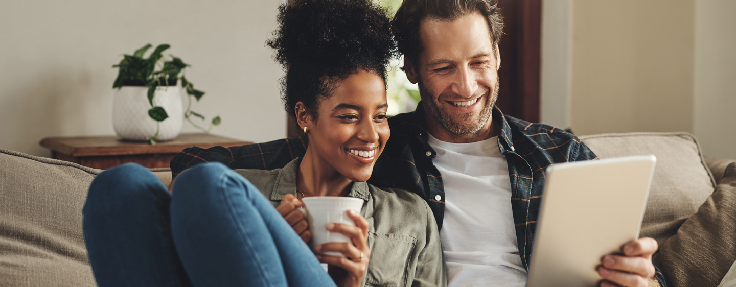 A couple sits on a couch with a tablet.