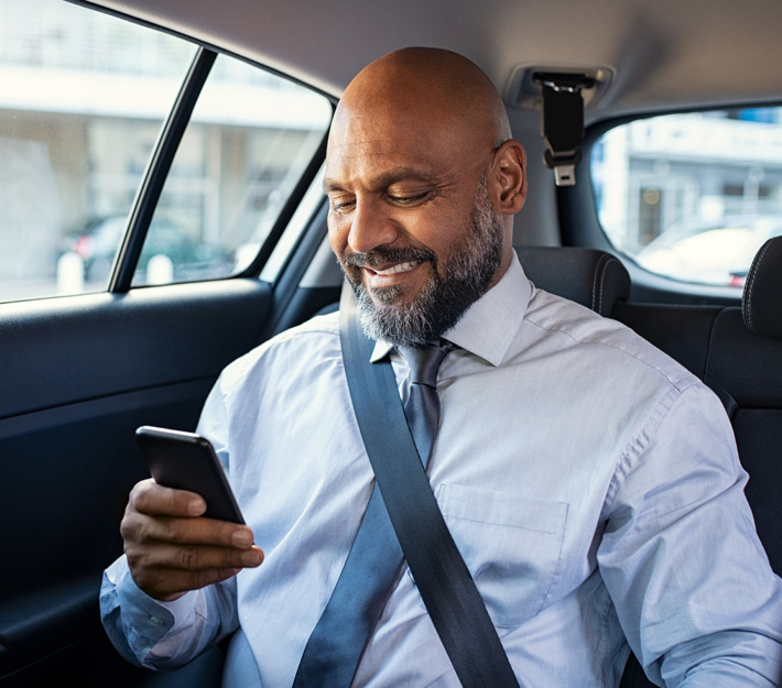 Man in the back of a car smiles at his cell phone.