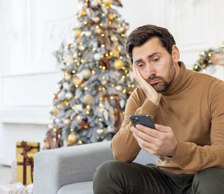 Man sitting on a couch with his face leaning on his hand, staring at his phone dejectedly.