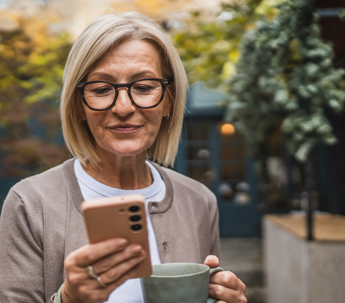 Image of older woman using her phone while holding a coffee mug
