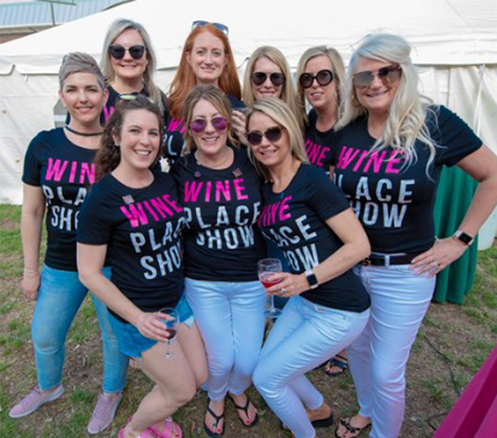 Group of women attending Winefest with shirts that say, "Wine. Place. Show."