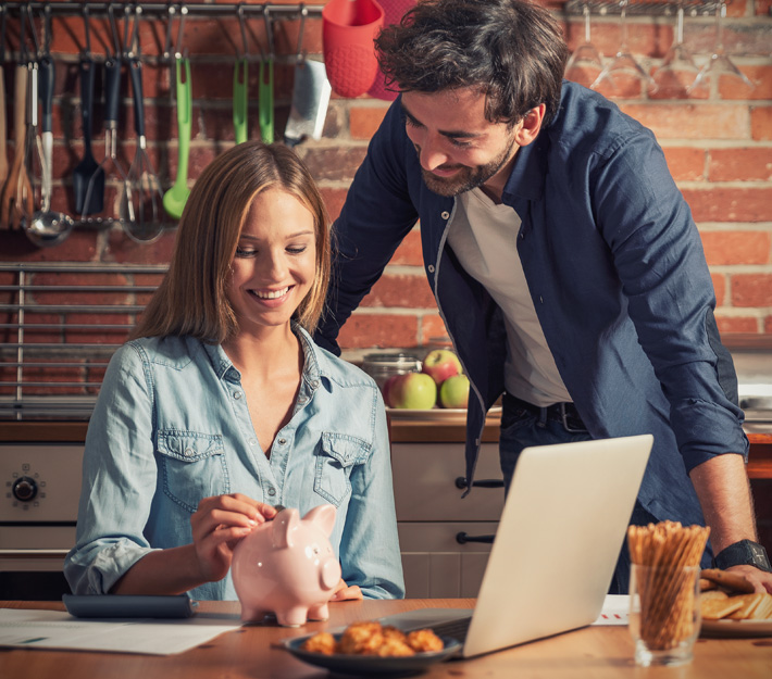 Man and woman in a kitchen with a laptop and a piggy bank.