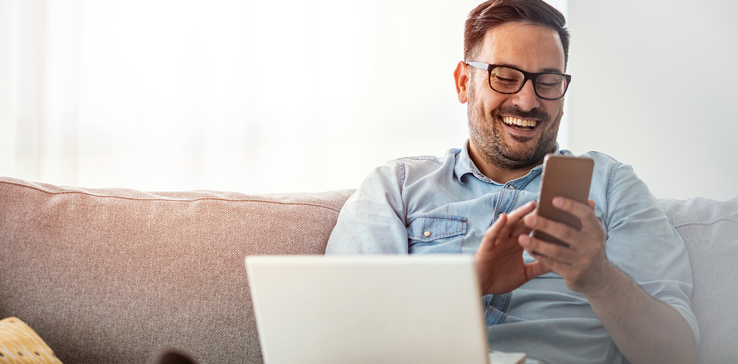 Man on phone, smiling, with laptop on lap.