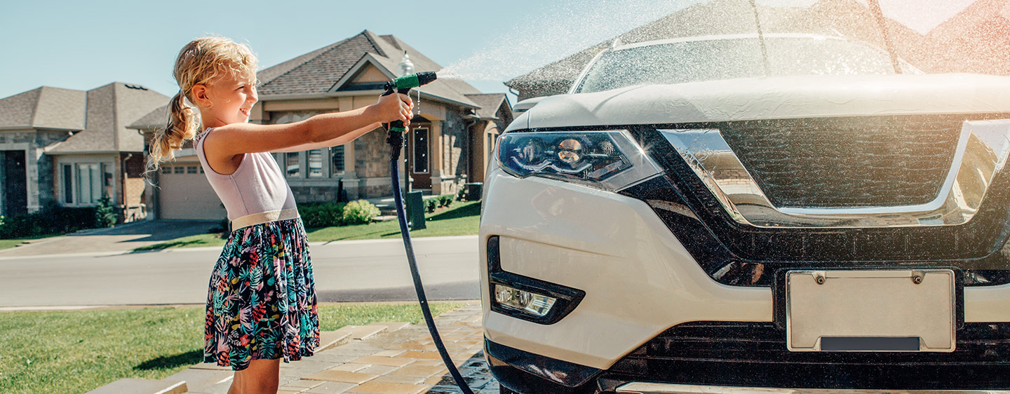 Young child spraying water house at car, washing it.