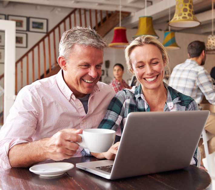 A couple in a coffee shop both looking at a laptop computer.