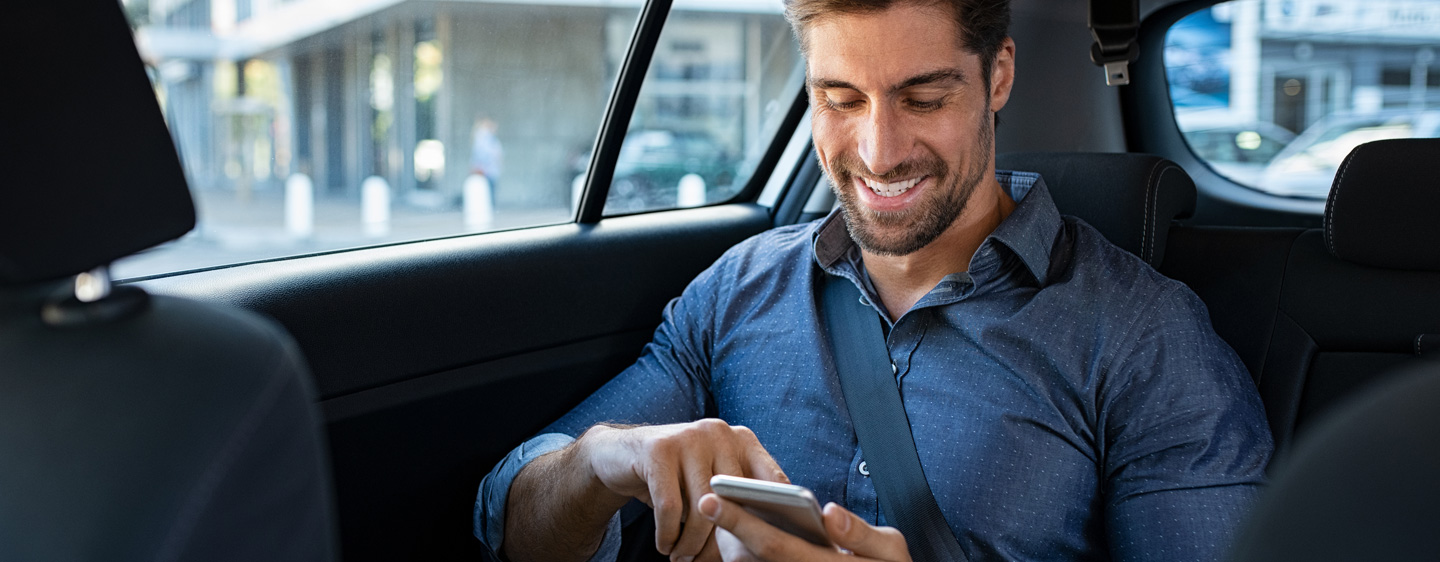 A man in the backseat of a car scrolls on his cellphone.