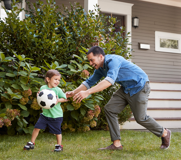 A dad and his son play in front of a home.