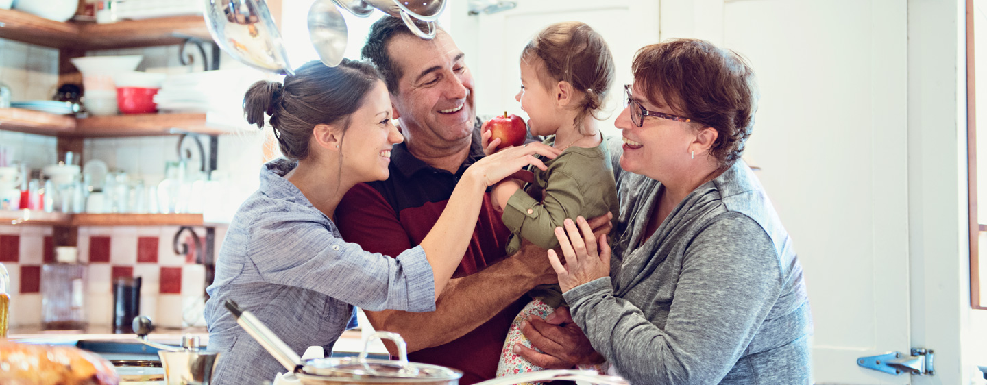 Grandparents hold their grandchild and chat with their daughter.