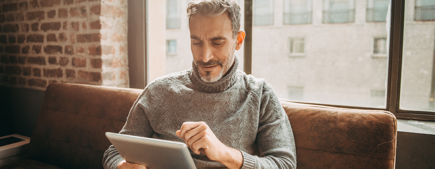 Man on a couch uses a tablet.