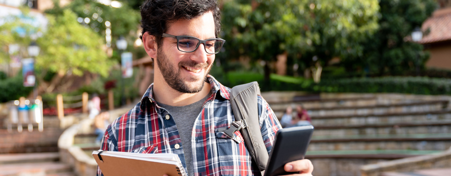 Student on campus smiles at his phone.