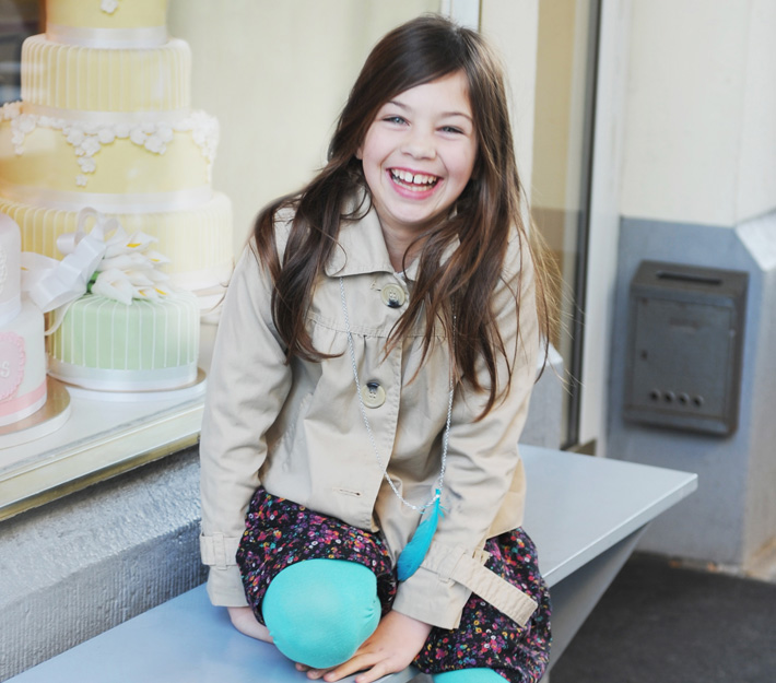 Smiling girl sits outside of a cake shop.