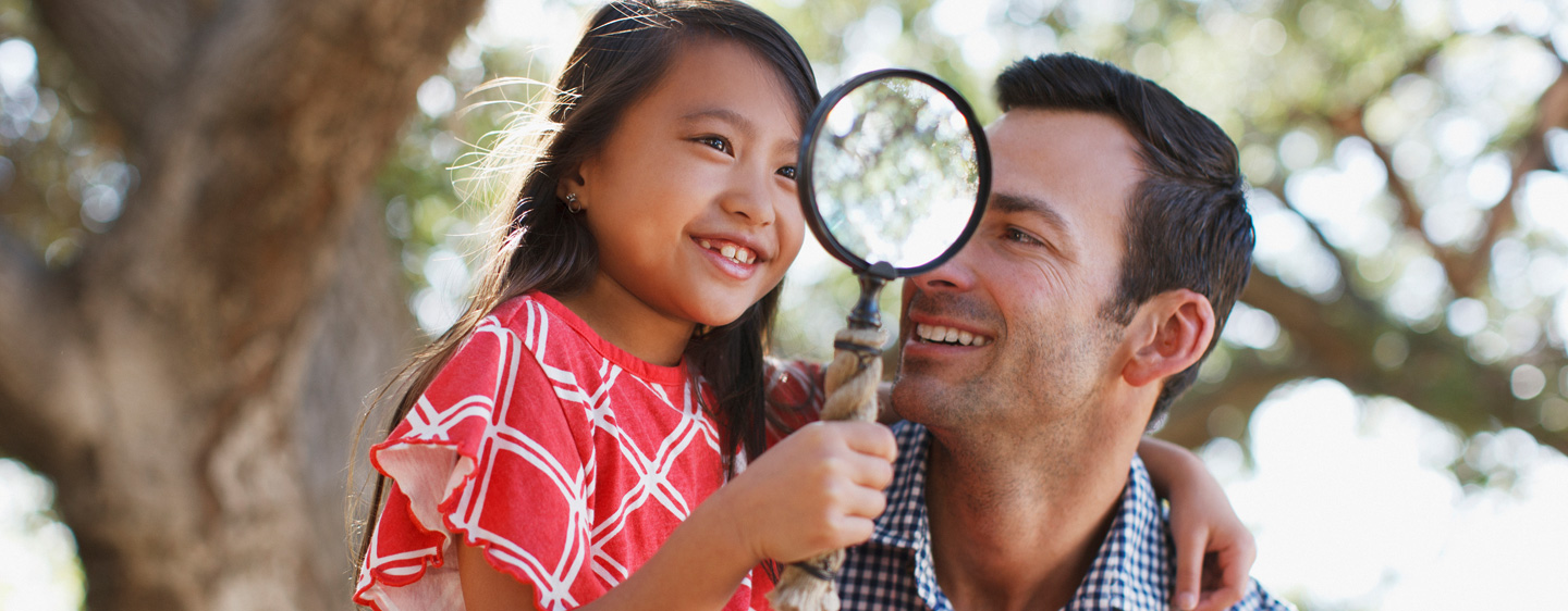 Man and daughter look through a magnifying glass.